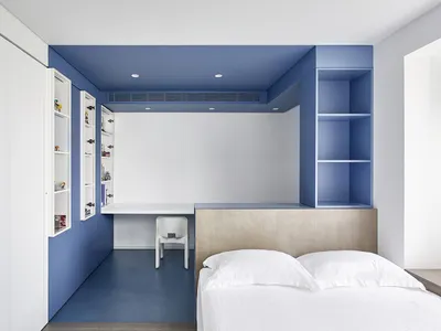 A minimalist bedroom with blue and white color scheme and a built-in desk.