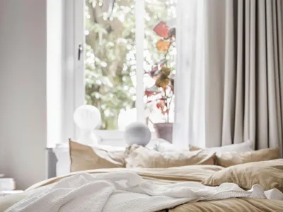 A minimalist bedroom with a bed covered in tan-colored cotton towels. White slippers are placed on the floor.