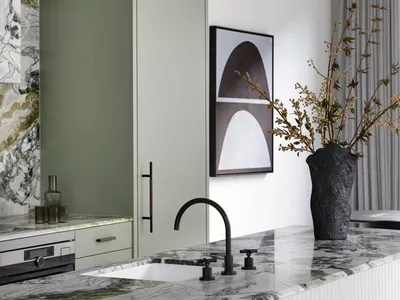A modern minimalist kitchen features a white and green marble countertop, with a black faucet and contemporary green cabinetr
