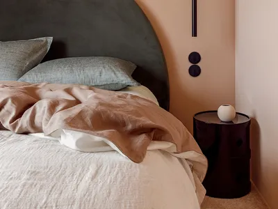 A minimalist bedroom with a gray upholstered headboard, soft textiles, and a sleek side table against a pastel wall.