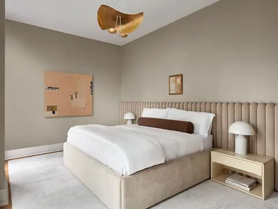 A minimalist bedroom with a white upholstered bed, beige upholstered headboard, and modern white table lamps.