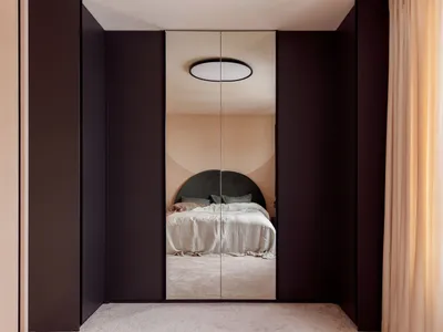 A modern minimalist bedroom featuring a black feature wall, white bed, and carpeted floor.
