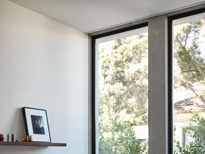 Modern home office featuring a wooden desk, minimalist chair, and large window with views of greenery.