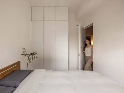 A minimalist bedroom featuring white wooden furniture and white walls.