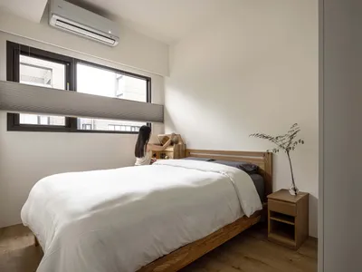 A minimalist bedroom featuring a wooden bed and furniture, with a woman organizing items on the bed.