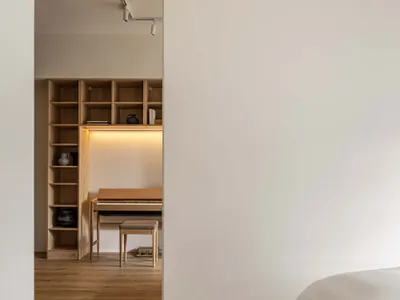 一間現代臥室，木質床架靠著白牆，旁有木質置物架與鋼琴。