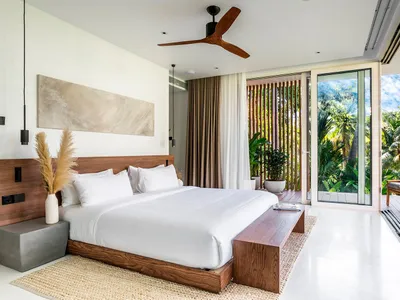 A minimalist bedroom with a wooden bed frame, white bedding, and large windows overlooking lush greenery.