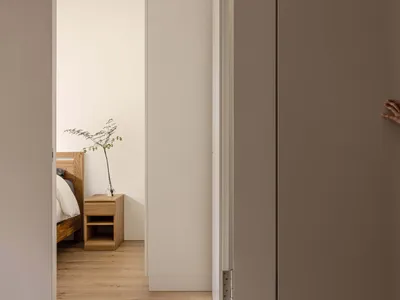 A minimalist bedroom with a white floor, wooden bed, and glass side table.