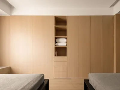 A modern minimalist bedroom with wooden paneling, featuring two beds and a built-in wardrobe.