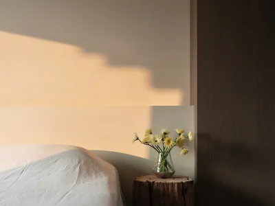 A minimalist bedroom featuring a wooden log nightstand with a vase of flowers.