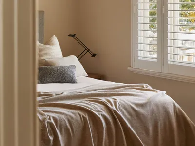 Minimalist bedroom featuring a bed with a lamp and window shutters.