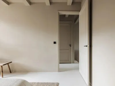 A minimalist bedroom with a concrete floor and white walls, featuring a simple wooden bench.
