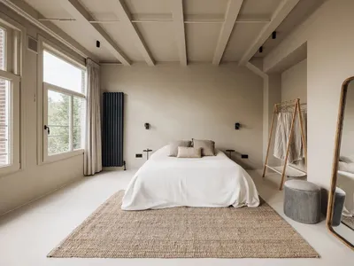 A minimalist bedroom with neutral tones and a white bed, featuring a wooden mirror and a textured rug.