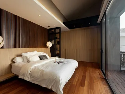 Modern minimalist bedroom with white bedding, wood-paneled walls, and floor-to-ceiling windows.