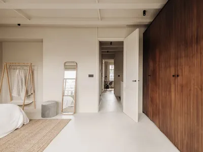 A minimalist bedroom with white walls, a white bed, and wooden closet doors.