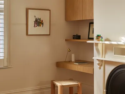 A minimalist home office featuring a wooden desk, shelves, and a stool under a pendant lamp, with a warm, cozy atmosphere.