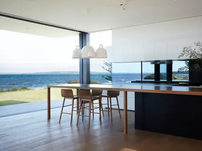 Modern kitchen with wooden table, glass pendant lights, and ocean view.
