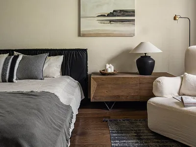 Modern, minimalist bedroom featuring a black upholstered bed and a wooden sideboard with a table lamp.