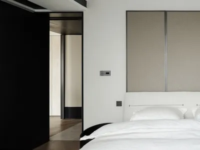 Modern minimalist bedroom with white bed, neutral-toned fabric wall panels, and black trim.
