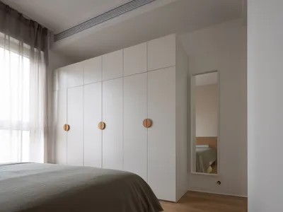 A minimalist bedroom with white walls, wooden floors, and a large window with sheer curtains.
