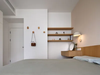 A minimalist bedroom with a bed, hanging bag, floating shelves, and a white door.