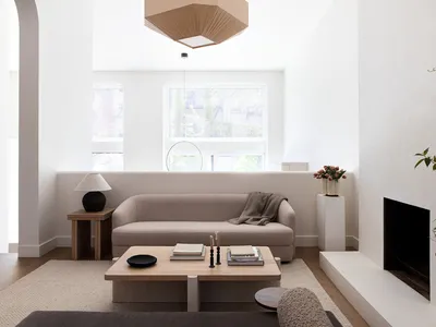 Modern, minimalist living room with light-colored fabric sofa, wooden coffee table, concrete fireplace, and large windows.