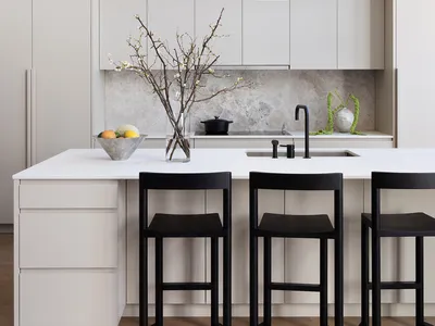A minimalist kitchen with white cabinets, a white countertop, and black stools.