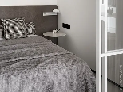 Modern minimalist bedroom with white walls, a grey fabric bed, and textured bedding, featuring a glass closet door.