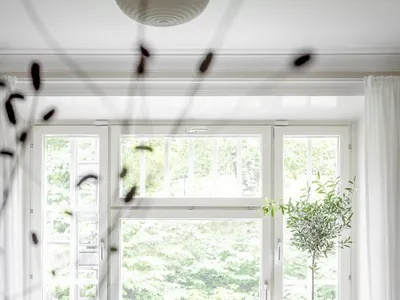 White couch, beige cushions, potted plants, candles, white curtains, and large window