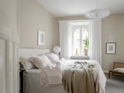 A minimalist bedroom with fabric bedding and wooden furniture, featuring an arched window and a plant on the windowsill.