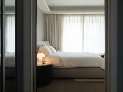 A minimalist bedroom featuring a white fabric bed with soft lighting and light-colored wooden furniture.