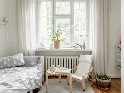 A minimalist bedroom with wooden furniture, white fabrics, and green plants.