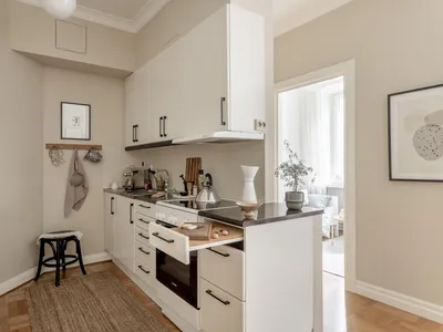 A spacious, modern, minimalist kitchen with white cabinets, a wood floor, and beige walls.