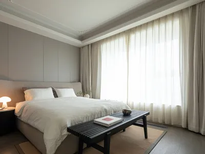 A minimalist bedroom designed with gray and taupe tones, featuring a large bed with soft bedding, a side table with a table l