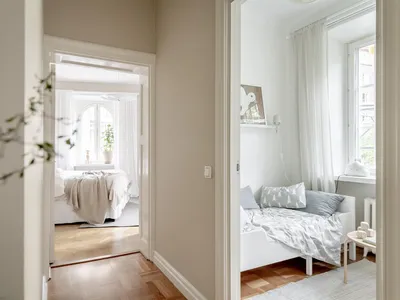 A modern minimalist bedroom with white furniture and wooden floors.
