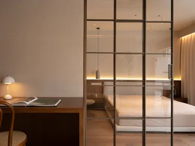 A minimalist bedroom featuring a wooden desk with a table lamp and an open book.
