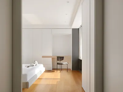 A minimalist bedroom with white walls, a wooden floor, and furniture.