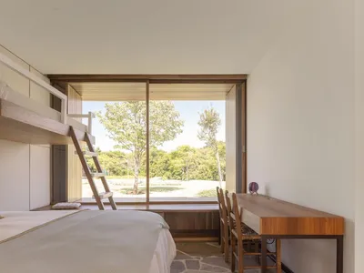 Minimalist bedroom with wooden furniture, including a bunk bed and a desk with chairs.