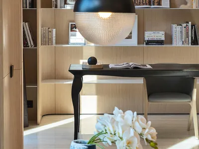 Modern home office featuring a wall of built-in bookshelves and wood furniture, with a pendant light fixture hanging above a