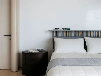 A minimalist bedroom featuring a bed with a wooden headboard, a metal shelf, and fabric bedding.