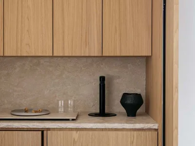 A minimalist kitchen features wooden cabinets and a marble countertop with a sleek black faucet and decorative black vase.
