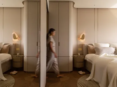 A modern bedroom with neutral-toned walls, flooring, and furnishings, featuring two beds, wall sconces, and a large closet.