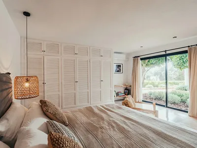 Minimalist bedroom with white walls, furniture, and neutral-toned bedding.