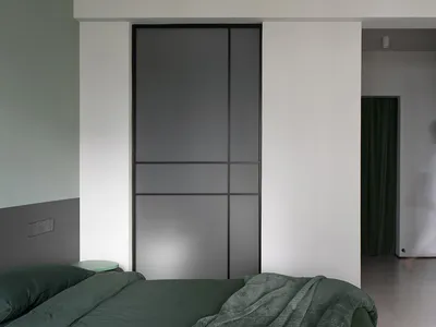 Minimalist bedroom with green bedding, black metal sliding doors, and white walls.