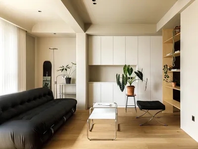 Modern minimalist living room with a black leather sofa, wooden flooring, and white cabinets.