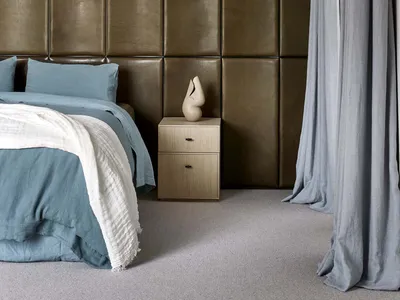 A modern minimalist bedroom featuring a large bed with blue bedding, a side table with a sculpture, and a leather accent wall