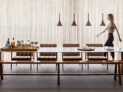 A contemporary restaurant dining room featuring wooden furniture, upholstered seats, and glass pendant lights.