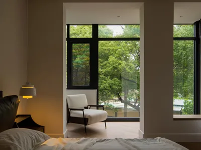 A cozy, minimalist bedroom with a white fabric armchair overlooking green trees.