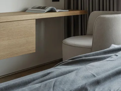 Open book on a modern minimalist bedside table with a wooden desk and upholstered chair.