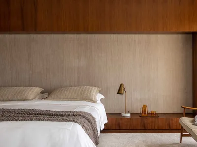 Minimalist bedroom featuring a bed with a textured headboard and wooden paneling, complemented by a carpeted floor and fabric